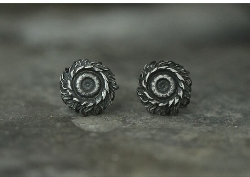 May include: A pair of silver earrings with a detailed, circular design resembling a stylized flower or sun. The center of each earring features a smaller circle.