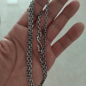 Op de afbeelding: Een zilveren ketting met een karabijn sluiting. De ketting is gemaakt van kleine, met elkaar verbonden vierkanten.