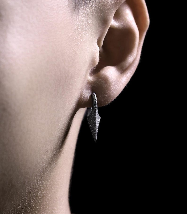 May include: A silver earring with a pointed, triangular design. The earring is worn in the left earlobe.