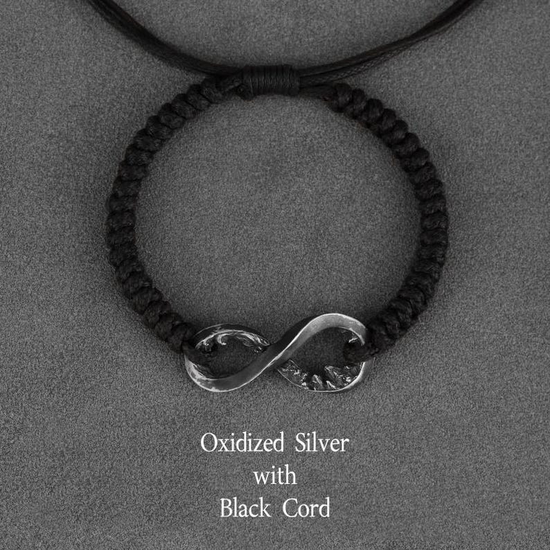 May include: A black cord bracelet featuring an oxidized silver infinity symbol. The bracelet is made of a woven black cord and has the text "Oxidized Silver with Black Cord".
