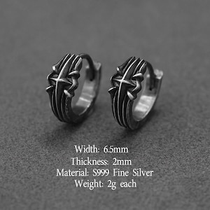 May include: A pair of S999 fine silver hoop earrings featuring a raised cross design with an oxidized finish. The earrings have a width of 6.5mm, a thickness of 2mm, and a weight of 2g each. The metal surface displays intricate carved detailing.