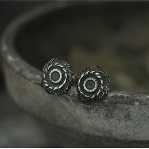 May include: A pair of silver stud earrings with a circular design featuring a raised center and a textured outer edge.