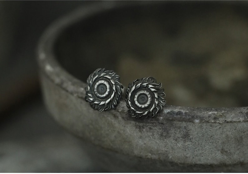 May include: A pair of silver stud earrings with a circular design featuring a raised center and a textured outer edge.