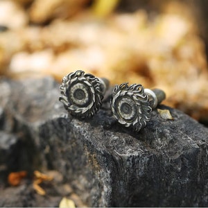 May include: Two silver earrings with a detailed design of a sun with rays. The earrings are on a dark gray rock.