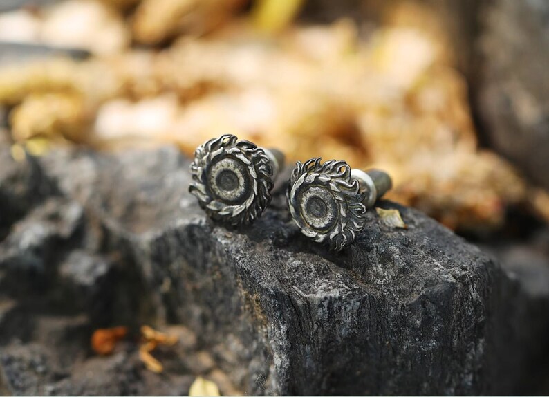 May include: Two silver earrings with a detailed design of a sun with rays. The earrings are on a dark gray rock.