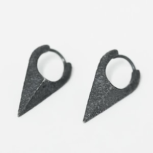 May include: A pair of black hoop earrings with a pointed triangular design. The earrings have a textured finish.