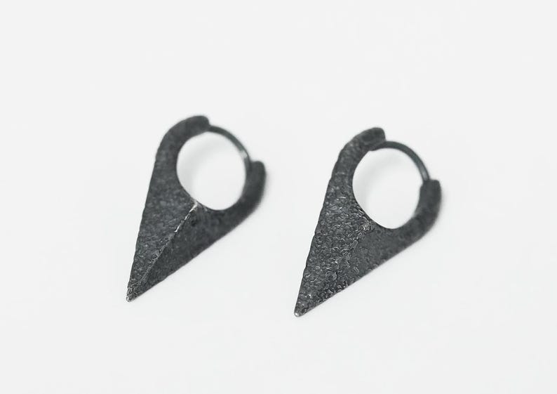 May include: A pair of black hoop earrings with a pointed triangular design. The earrings have a textured finish.