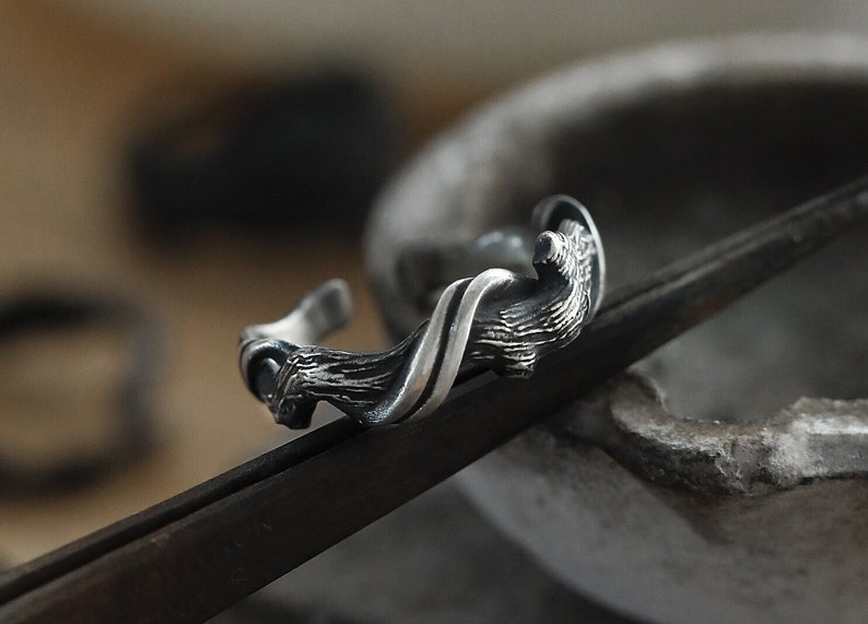 Pu&ograve; includere: Un bracciale a polsino argentato con un design organico e strutturato. Il bracciale presenta una forma scolpita e fluida con una texture dettagliata simile alla corteccia. Il design aperto del bracciale &egrave; visibile.