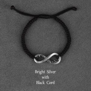 May include: A black cord bracelet featuring a bright silver infinity symbol. The text "Bright Silver with Black Cord" is displayed below the bracelet. The bracelet is adjustable.