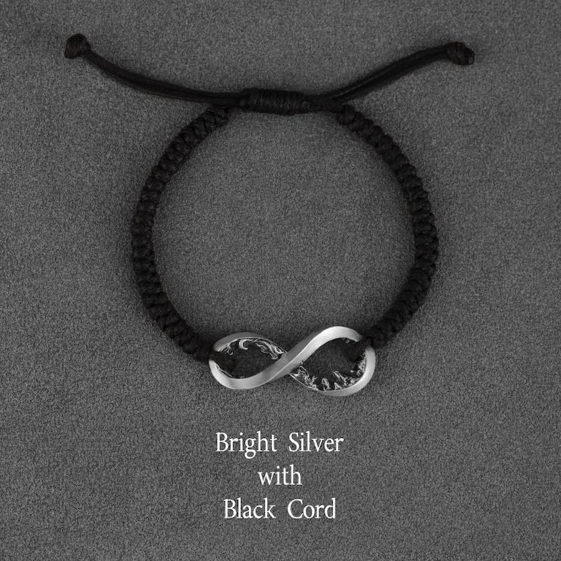 May include: A black cord bracelet featuring a bright silver infinity symbol. The text "Bright Silver with Black Cord" is displayed below the bracelet. The bracelet is adjustable.