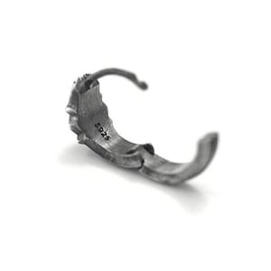 May include: A dark silver-toned hoop earring with a textured, rugged surface. The interior of the hoop is clearly stamped with the text S925, indicating the material composition. The earring features a hinged closure mechanism for secure fastening.