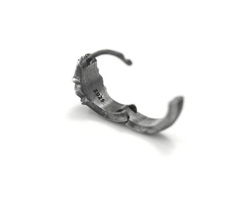 May include: A dark silver-toned hoop earring with a textured, rugged surface. The interior of the hoop is clearly stamped with the text S925, indicating the material composition. The earring features a hinged closure mechanism for secure fastening.