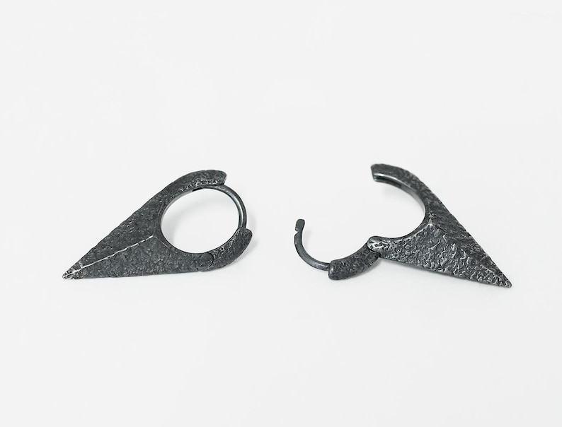 May include: A pair of silver hoop earrings with a pointed, textured design. The earrings are made of metal and have a hammered finish.
