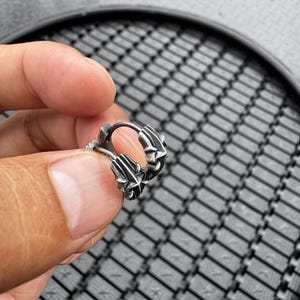 May include: A small silver hoop earring featuring a textured, multi-faceted design with pointed, star-like details along the outer edge. The metal has a darkened, oxidized finish in the recessed areas, highlighting the intricate, geometric relief pattern.