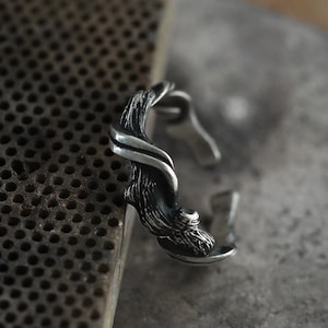 Pu&ograve; includere: Un anello argentato con un design ispirato alla natura. L'anello presenta una struttura strutturata a forma di ramo che si avvolge attorno al dito. Il design include dettagli intricati e una finitura lucida.