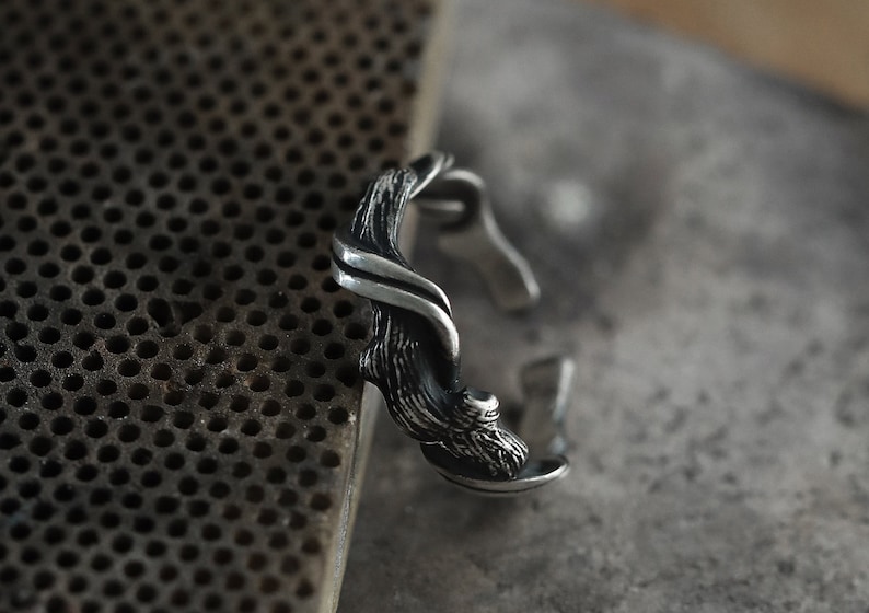 Pu&ograve; includere: Un anello argentato con un design ispirato alla natura. L'anello presenta una struttura strutturata a forma di ramo che si avvolge attorno al dito. Il design include dettagli intricati e una finitura lucida.