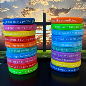 Puede incluir: Apilados brazaletes de silicona coloridos con texto blanco. Las pulseras son de varios colores, incluyendo azul, rosa, amarillo y verde. Cada pulsera presenta una cita inspiradora diferente. Una cruz negra se encuentra en el fondo.