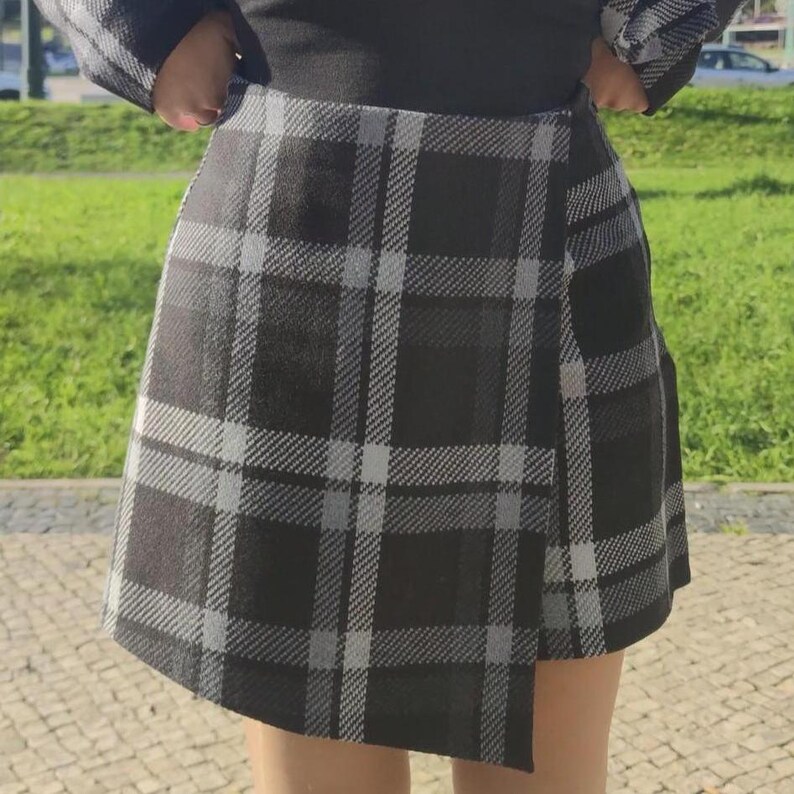 May include: A black and white plaid skirt with a wrap-around design. The skirt is short and has a casual style.