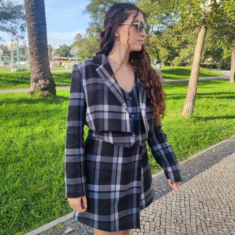 May include: A black and white plaid cropped blazer and matching skirt set. The blazer has a button closure and the skirt has a wrap style.