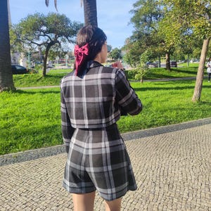 May include: A black and white plaid cropped jacket and matching shorts set. The jacket has long sleeves and a collar. The shorts are a-line and have a high waist. The set is worn by a person with a red bow in their hair.