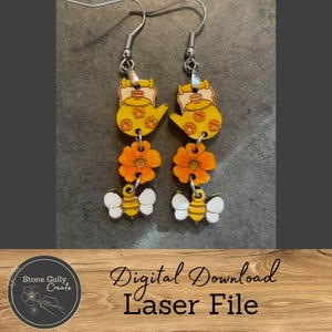 May include: A pair of dangle earrings with a nature theme. Each earring features a yellow teapot, orange flower, and a bee with white wings and yellow stripes. The earrings are made of wood and have silver-colored hooks.