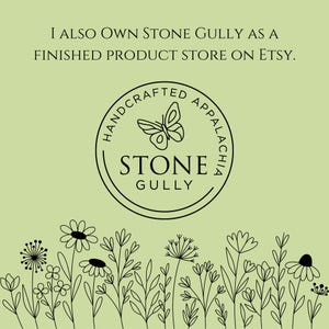 以下が含まれることがあります： 蝶と「ストーン・ガリー」の文字が描かれた、ストーン・ガリー・ハンドクラフト・アパラチアのための白黒のロゴ。「ハンドクラフト・アパラチア」の文字が書かれた円に囲まれています。ロゴは、花と植物の黒い線画の縁取りが施された薄い緑色の背景に配置されています。