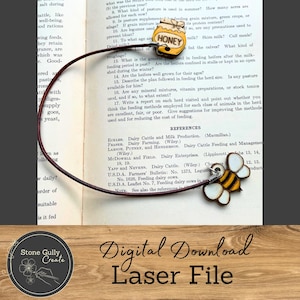 以下が含まれることがあります： 茶色の革紐に付けられた、木製のハチミツの壺のチャームとハチのチャーム。ハチミツの壺のチャームは黄色に塗られており、赤と白のラベルには「HONEY」と書かれている。ハチのチャームは黄色と黒に塗られており、白い羽根が付いている。