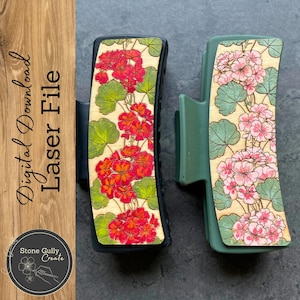 May include: Two hair clips with floral designs. The clip on the left is black with red flowers and green leaves. The clip on the right is green with pink flowers and green leaves. Both clips have a wood-like texture.