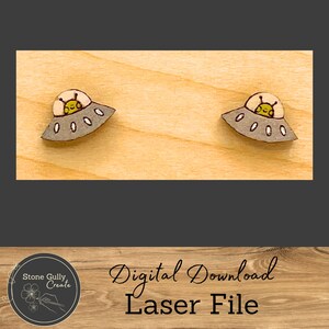 May include: Two wooden alien spaceship earrings. Each earring features a gray saucer with a yellow alien inside. The earrings are on a light wood surface. The image also includes the text "Digital Download Laser File".