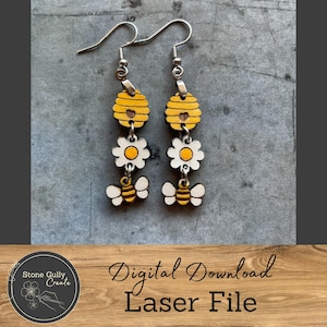 May include: A pair of laser cut wooden earrings featuring a bee, flower, and honeycomb design. The earrings are yellow, white, and brown.
