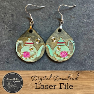 May include: Wooden teardrop earrings featuring a teal teapot design with pink roses and yellow bees. The earrings have silver-colored fish hook ear wires. The earrings are a digital download laser file.