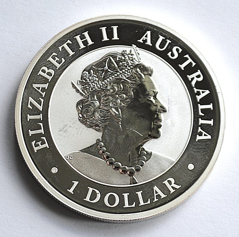 May include: A silver Australian 1 Dollar coin. The coin features a profile of Queen Elizabeth II, with the words "ELIZABETH II AUSTRALIA" and "1 DOLLAR" inscribed around the edge. The coin has a detailed design and a shiny finish.