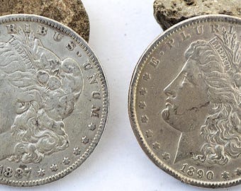 Op de afbeelding: Twee zilverkleurige Morgan dollar-munten met het profiel van Lady Liberty naar links gericht, met de tekst E PLURIBUS UNUM, LIBERTY en de jaartallen 1887 en 1890 op de voorzijde, omringd door een rand van dertien sterren.