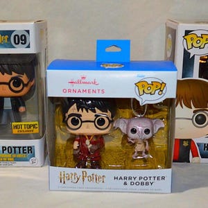 May include: Three Funko Pop Harry Potter vinyl figures in original packaging. Two boxes contain individual Harry Potter figures numbered 09 and 10. The center box is a Hallmark ornament set featuring a Harry Potter figure and a Dobby figure.
