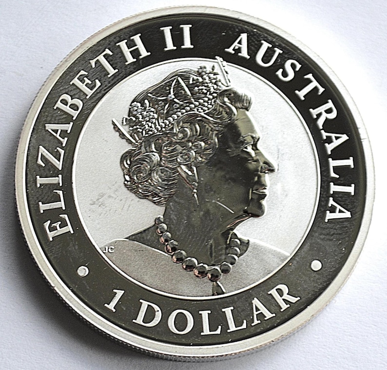 May include: A silver Australian 1 dollar coin. The coin features a profile of Queen Elizabeth II, the words "ELIZABETH II AUSTRALIA" and "1 DOLLAR" are inscribed around the edge. The coin has a detailed design.