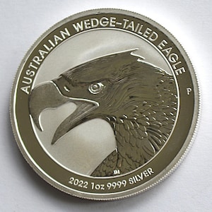 May include: A silver coin featuring a detailed profile of an eagle's head with an open beak. The coin's edge has a textured design. The text "AUSTRALIAN WEDGE-TAILED EAGLE" arcs around the top, with "2022 1oz 9999 SILVER" at the bottom.