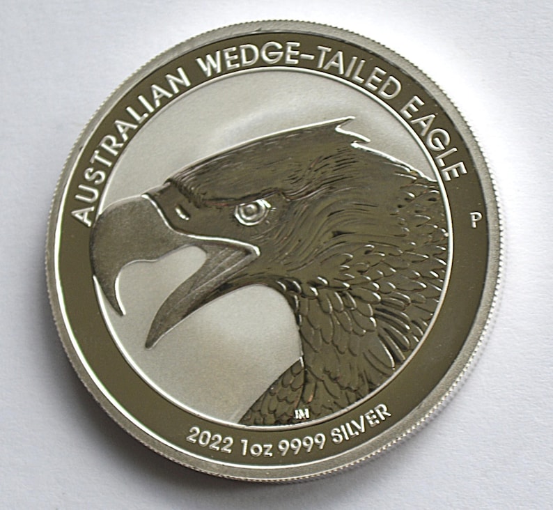 May include: A silver coin featuring a detailed profile of an eagle's head with an open beak. The coin's edge has a textured design. The text "AUSTRALIAN WEDGE-TAILED EAGLE" arcs around the top, with "2022 1oz 9999 SILVER" at the bottom.