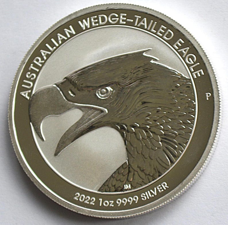 May include: A silver coin featuring a detailed profile of an eagle's head. The coin's edge is inscribed with "AUSTRALIAN WEDGE-TAILED EAGLE" and "2022 1oz 9999 SILVER". The eagle's beak is open, and the coin has a shiny finish.