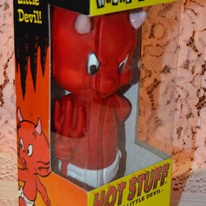 May include: A Hot Stuff Wacky Wobbler bobblehead figure inside a yellow and orange cardboard box with a clear plastic window. The red devil character wears a white diaper and holds a red trident. The box features the text Hot Stuff The Tuff Little Devil.