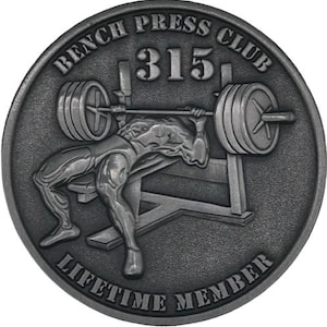 Peut inclure: Une pièce de monnaie en métal argentée avec un motif représentant une personne soulevant une barre de musculation. La pièce porte l'inscription "Bench Press Club 315 Lifetime Member" sur le bord.
