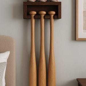May include: A wooden baseball bat and ball display. The dark brown wooden shelf holds three baseballs with red stitching. Three wooden baseball bats hang below. The display is mounted on a light gray wall.