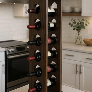 May include: A tall, vertical dark brown wooden wine rack with a square base. The rack features six circular cutouts on each side, holding twelve wine bottles with dark glass and various colored labels, arranged in a symmetrical grid pattern.