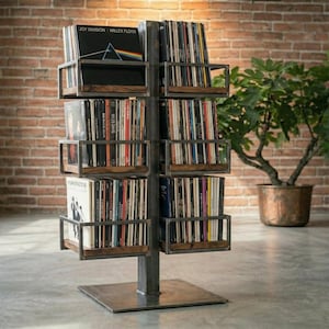 Könnte beinhalten: Ein Metall- und Holz-Schallplattenregal mit mehreren Regalen, die jeweils Schallplatten aufnehmen. Das Regal hat einen quadratischen Sockel und eine zentrale Stütze. Die Schallplatten sind sichtbar, mit nach außen gerichteten Albumcovern.