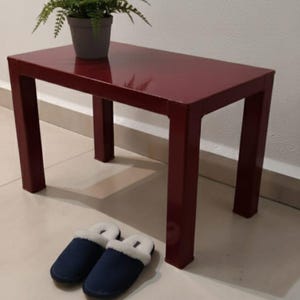 Könnte beinhalten: Ein burgunderfarbener rechteckiger Tisch mit vier Beinen, auf dem sich eine Topfpflanze und ein Paar marineblaue Hausschuhe befinden. Der Tisch ist etwa 76 cm lang.