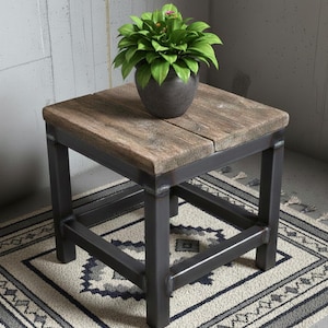 Könnte beinhalten: Kleiner, quadratischer Beistelltisch mit einer Tischplatte aus verwittertem Holz und einem dunklen Metallrahmen. Der Tisch ist 46 cm hoch und hat eine Topfpflanze mit grünen Blättern. Der Tisch steht auf einem gemusterten Teppich.