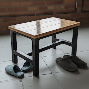 Op de afbeelding: Een rechthoekige houten bank met een natuurlijk afgewerkt blad en zwarte metalen poten. De bank is 76 cm lang, 38 cm breed en 46 cm hoog. Twee paar pantoffels zijn bij de bank geplaatst.