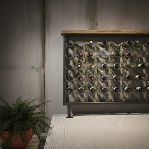 Op de afbeelding: Een metalen wijnrek met een houten bovenkant, met meerdere wijnflessen. Het rek heeft een donkergrijs frame en een decoratief kettingontwerp. Een potplant staat voor het rek.