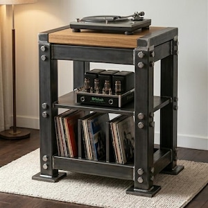 May include: A rustic, industrial-style record player stand. It features a wooden top, metal frame, and shelves for vinyl records and audio equipment. The stand is gray with visible bolts and rivets, and sits on a neutral-colored rug.
