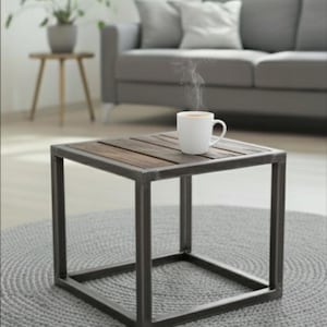 Peut inclure: Une table basse carrée avec un plateau en bois foncé et un cadre en métal. Une tasse blanche contenant une boisson chaude est posée sur la table, de la vapeur s'en échappe. La table est sur un tapis gris.