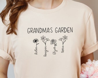 Può includere: Una maglietta beige chiaro con il testo "Grandma's Garden" e quattro fiori stilizzati con i nomi Aiden, Reagan, Elyzer e Nora scritti sotto.